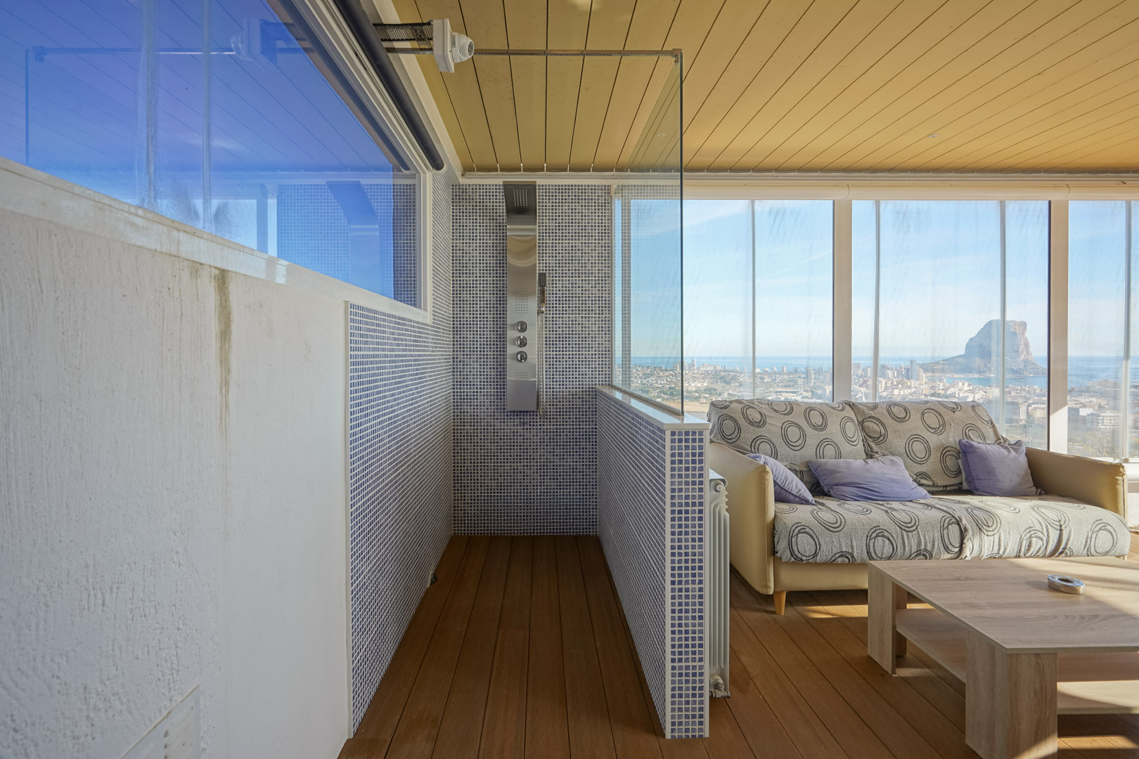 Wellnessruimte op de bovenverdieping met hydromassagedouche, blauwe mozaïektegels en glazen pui met panoramisch uitzicht op de Peñón de Ifach en de kust.