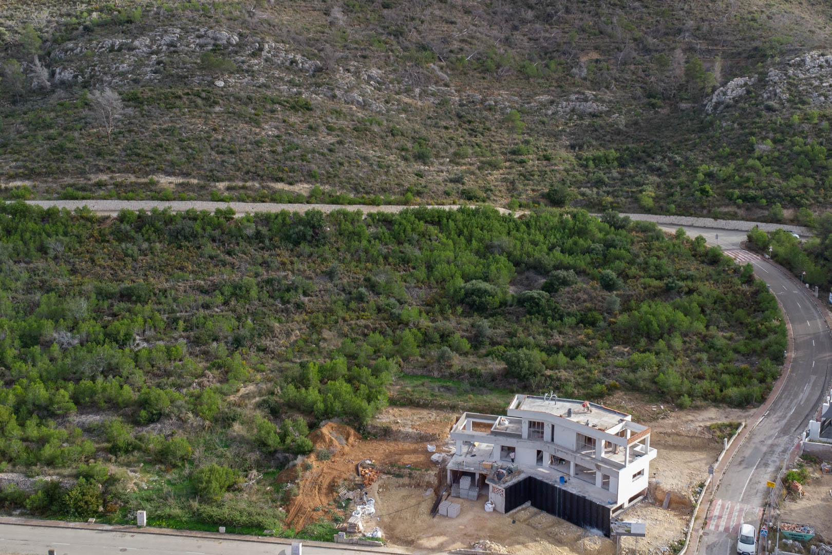 Luchtfoto van een villa in aanbouw in Monte Olímpico, Jávea, grenzend aan een mediterraan natuurgebied en volledig geasfalteerde wegen.