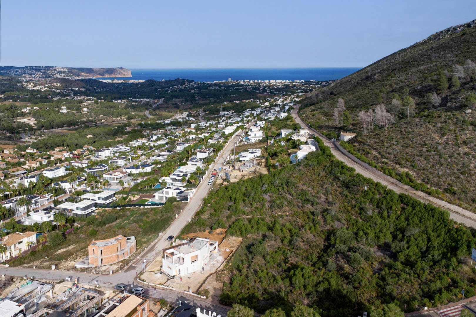 Luchtfoto van het bouwperceel in Monte Olímpico, Jávea, met uitzicht op een moderne woonwijk en de Middellandse Zee richting Cabo de San Antonio.