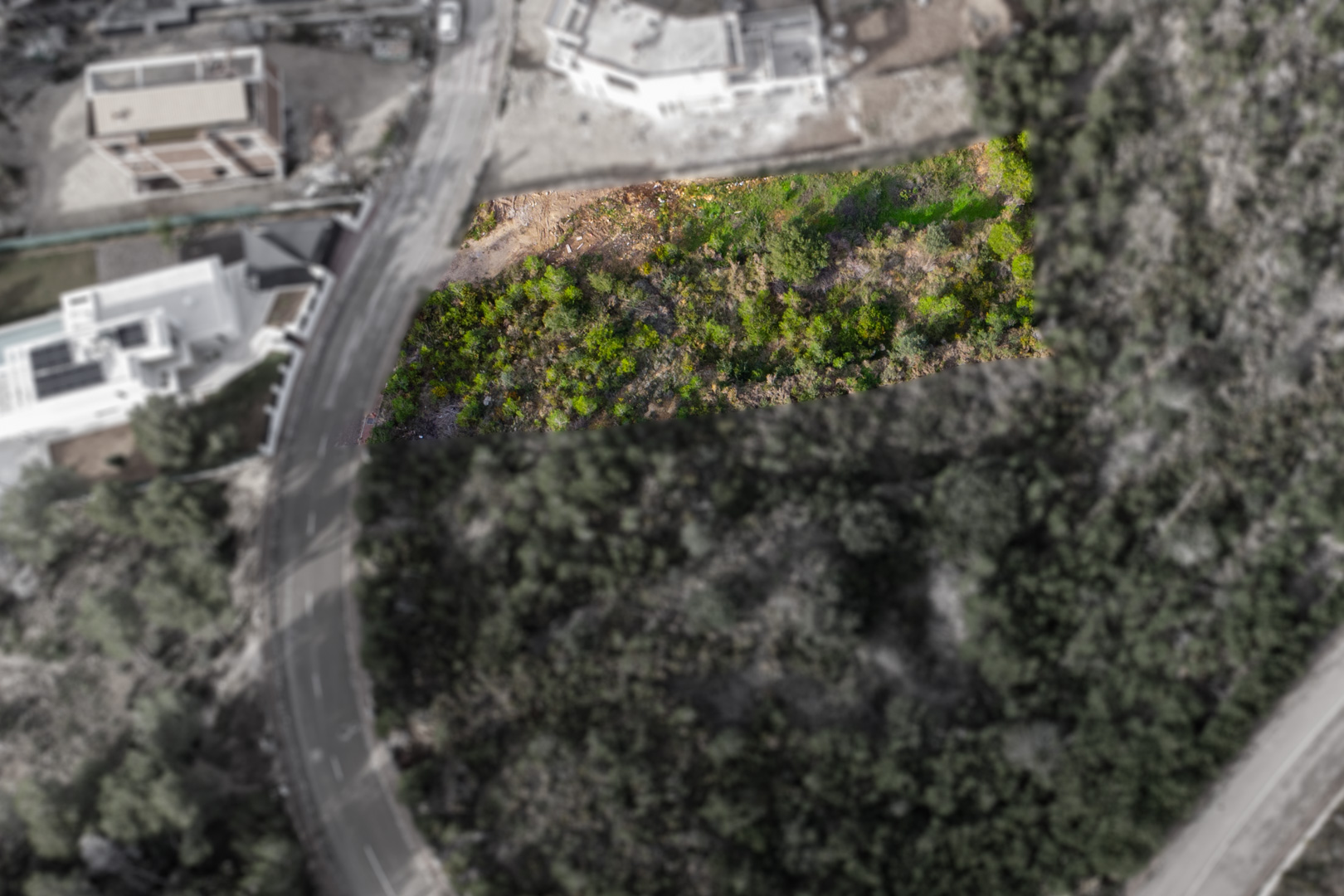 Luchtfoto van het gemarkeerde rechthoekige perceel, met natuurlijke begroeiing en directe toegang via een geasfalteerde weg in een ontwikkelde woonwijk.