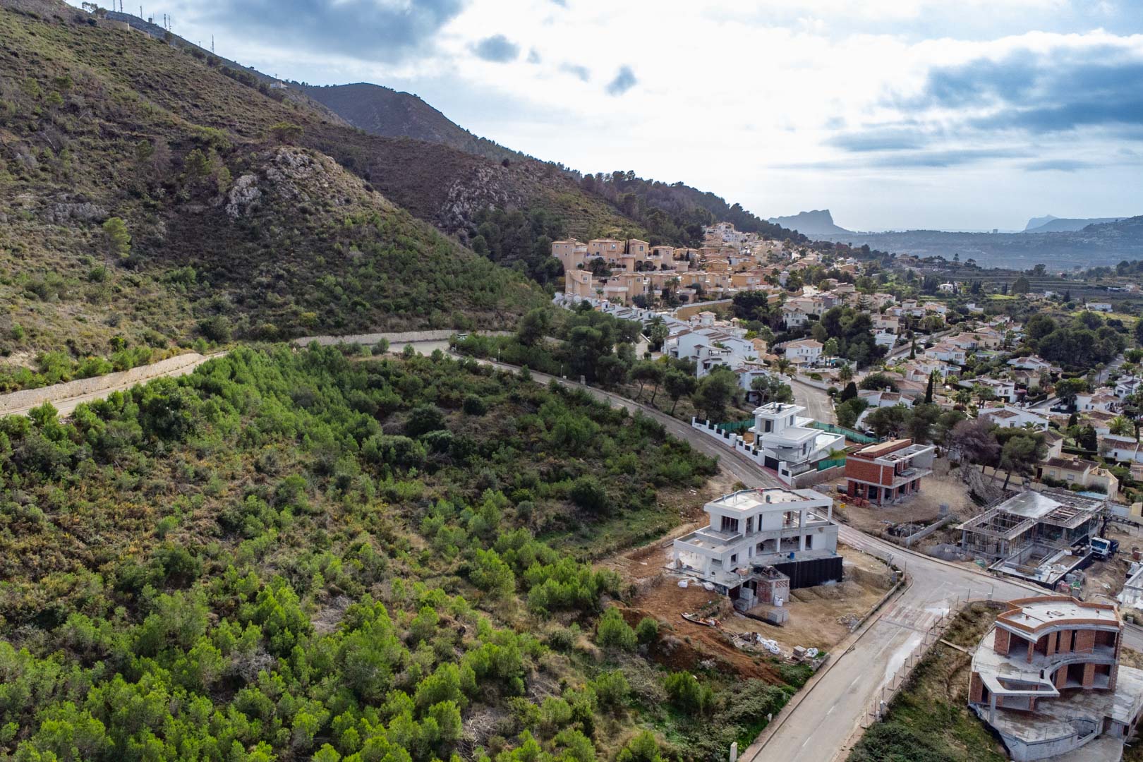 Luchtfoto van het perceel in Monte Olímpico, met geasfalteerde wegen, villa's in aanbouw en een panoramisch uitzicht over de groene heuvels en de vallei.