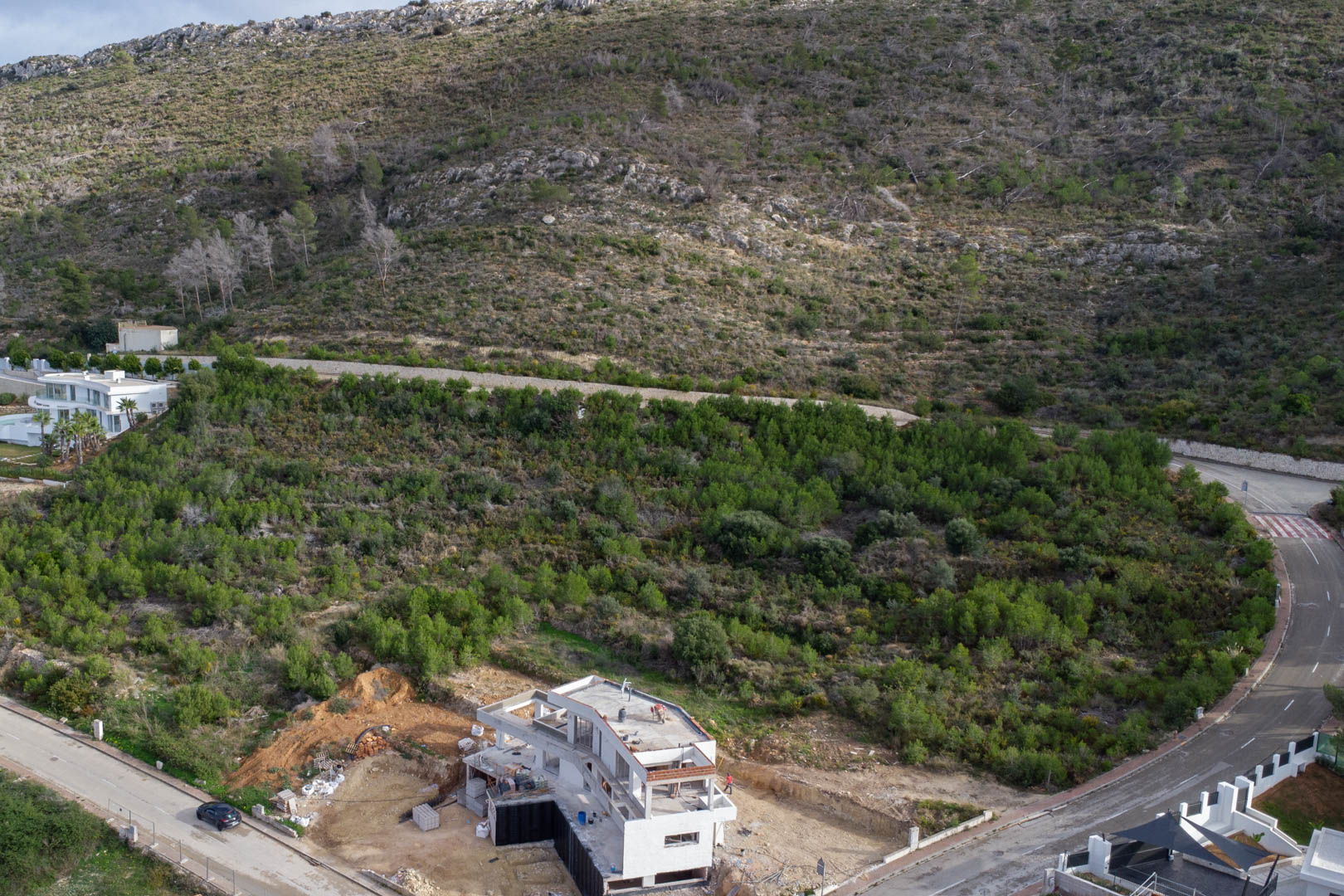 Luchtfoto van het perceel in Monte Olímpico, met voltooide stedelijke infrastructuur en een villa in aanbouw te midden van mediterrane begroeiing.