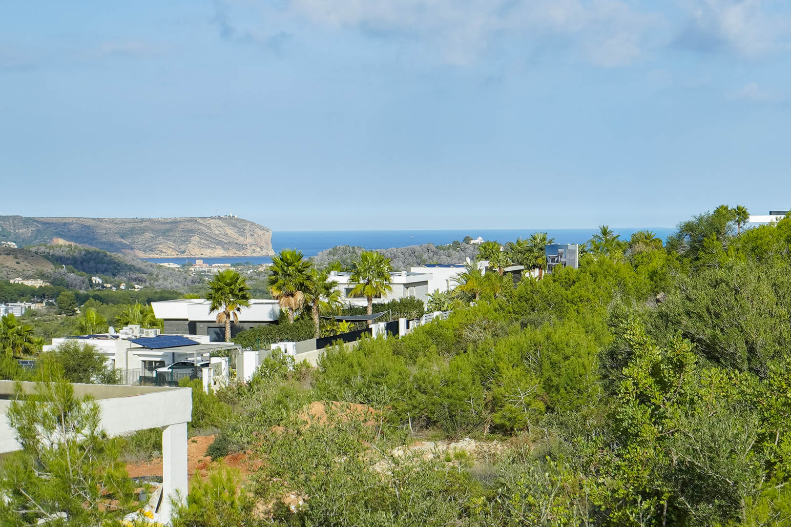 Panoramisch uitzicht op de Middellandse Zee en Cabo de San Antonio vanaf het perceel, omgeven door moderne villa's en weelderig mediterraan groen.