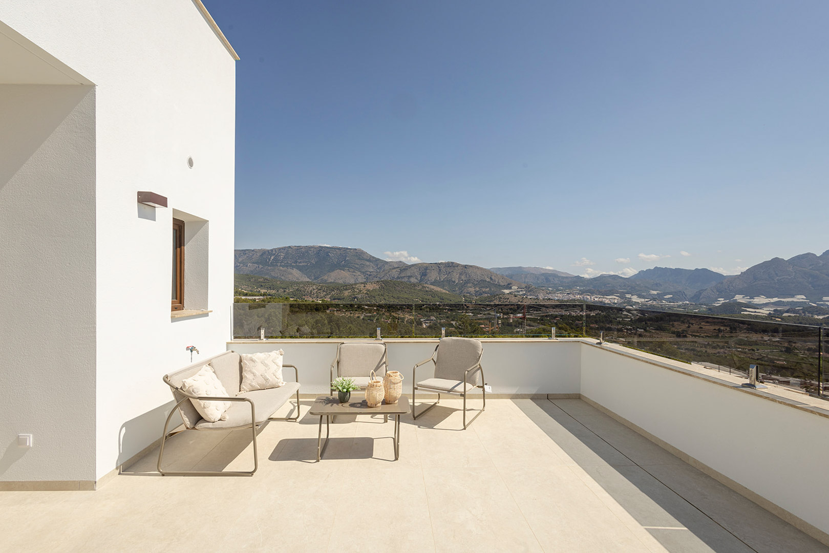 Bovenste terras met glazen balustrade en buitenlounge, met een onbelemmerd panoramisch uitzicht op de bergen en het omliggende landschap.