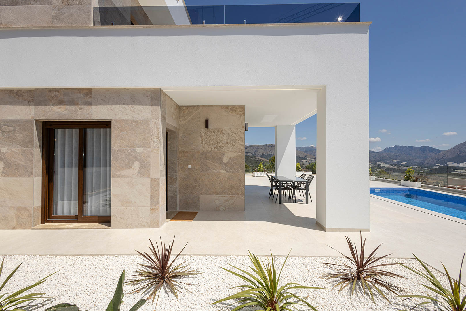 Moderne villa met natuurstenen gevelbekleding, overdekt terras met eethoek, privézwembad en panoramisch uitzicht op de bergen.