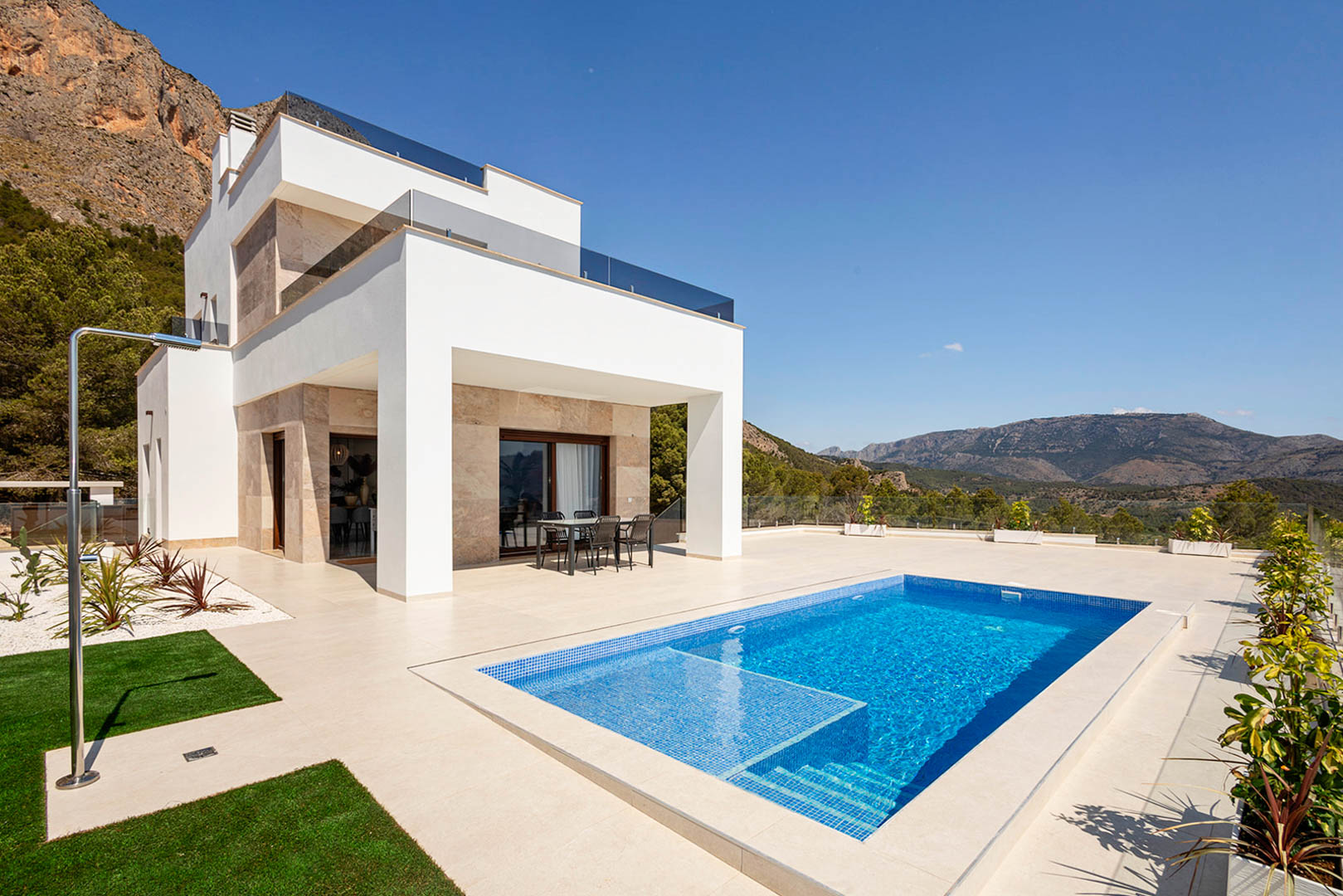 Moderne villa met witte gevels, natuurstenen accenten, privézwembad, buitendouche en een ruim terras met panoramisch uitzicht op de bergen.