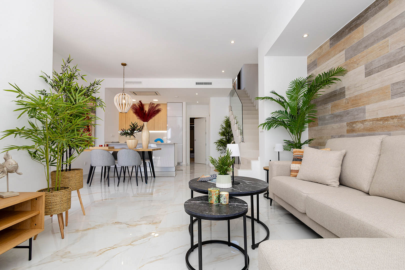 Open woonkamer met marmerlook porseleinen vloer, een houten accentwand en een moderne trap voorzien van een glazen balustrade.