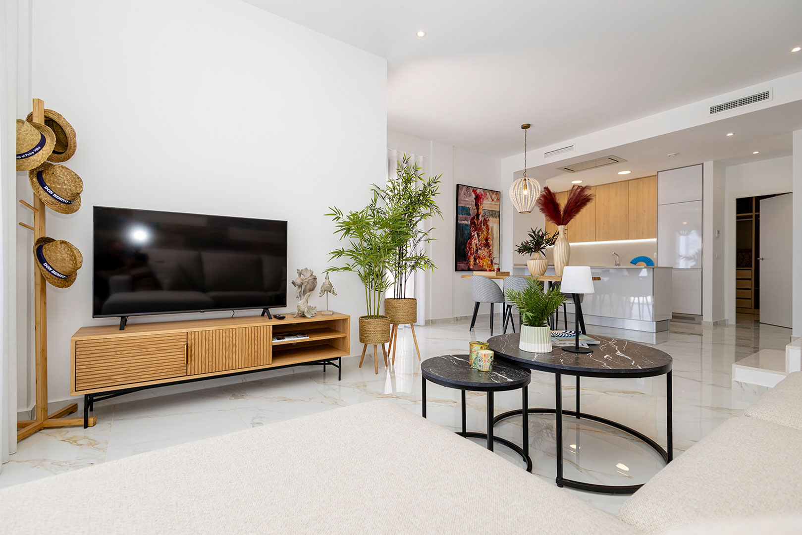 Open woonkamer met marmerlook porseleinen vloer, natuurlijk houten tv-meubel en een moderne keuken voorzien van een wit kookeiland en houten kasten.