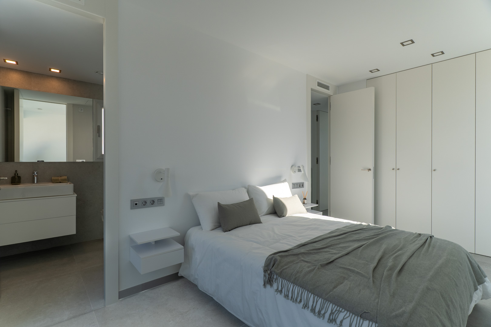 Hoofdslaapkamer met en-suite badkamer, kamerhoge inbouwkasten en een strak minimalistisch interieur met geïntegreerde plafondspots.