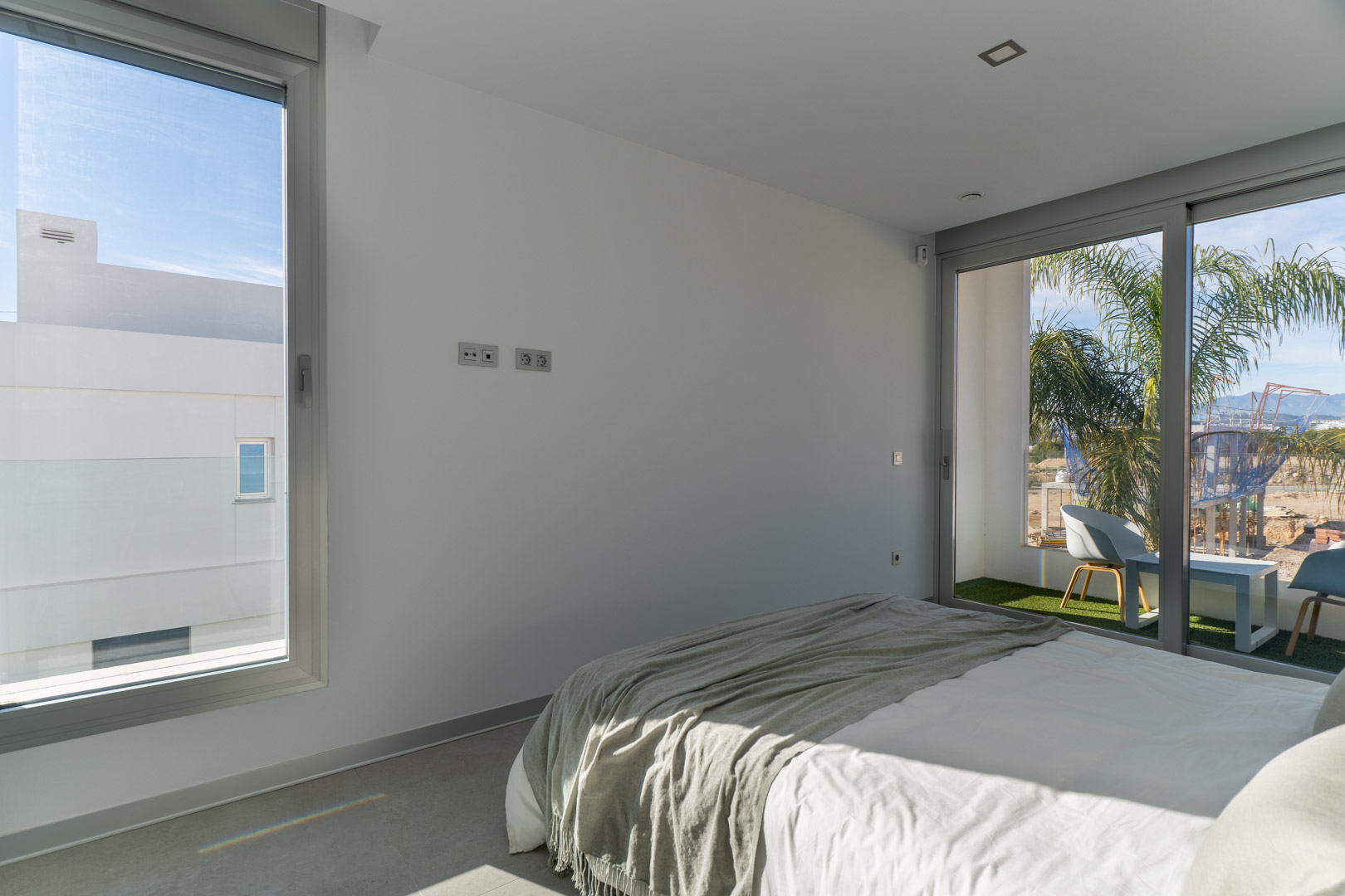 Lichte slaapkamer met directe toegang tot een privébalkon met kunstgras. Voorzien van een minimalistisch ontwerp, grijze tegelvloer en veel natuurlijk licht.