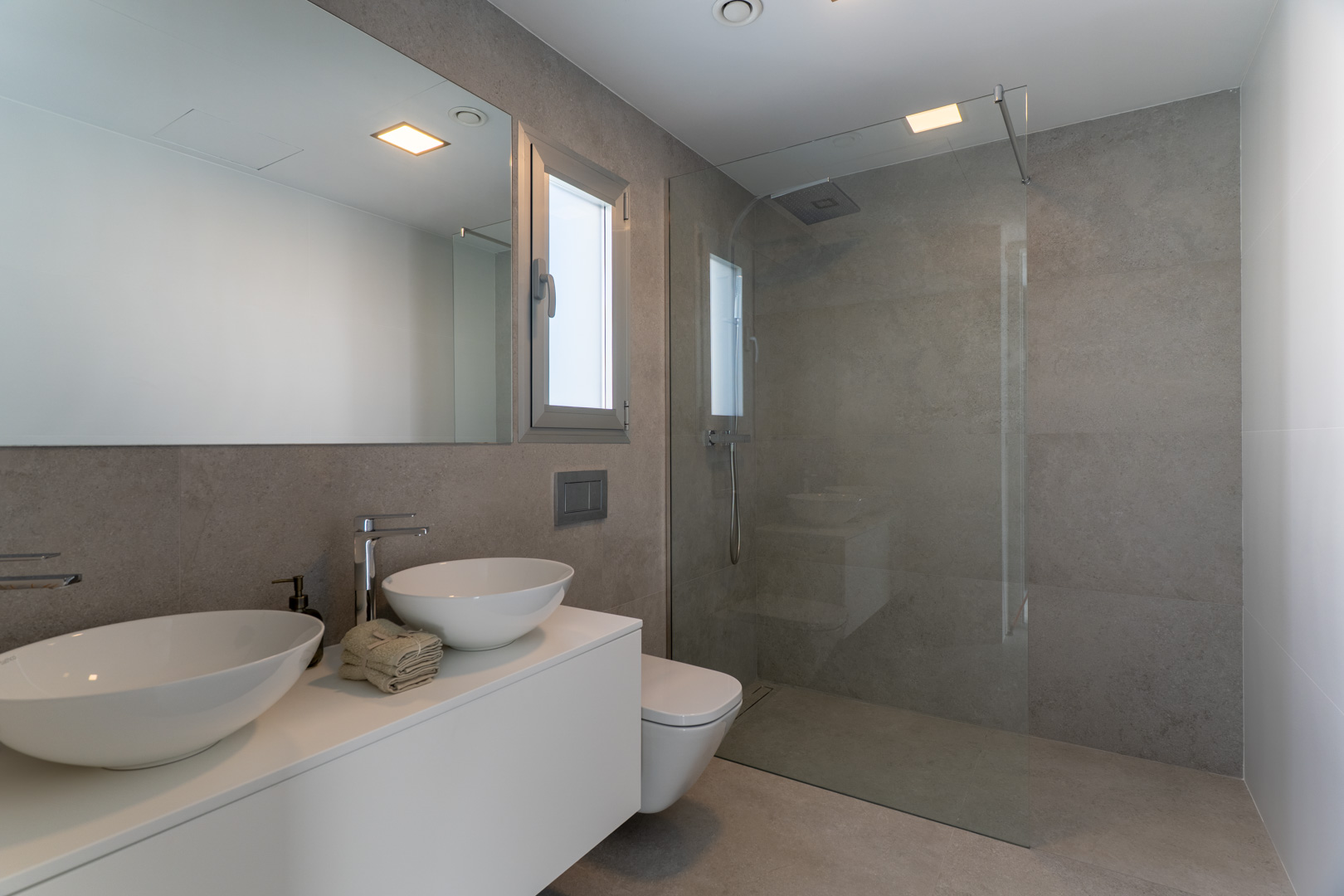 Moderne badkamer met grijze natuursteenlook tegels, dubbele wastafel op een zwevend wit meubel en een inloopdouche met glazen wand.