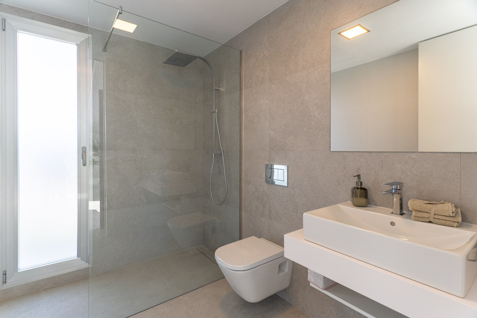 Moderne badkamer met grijze natuursteenlook tegels, een glazen inloopdouche, hangend toilet en een zwevend wastafelmeubel met een rechthoekige wasbak.