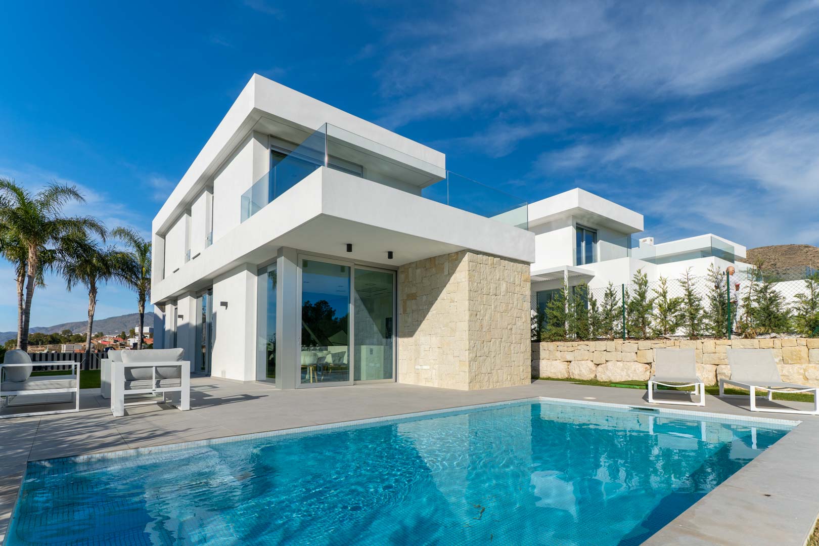 Moderne villa met privézwembad, minimalistische witte gevel, natuurstenen accentmuur en terrassen met glazen balustrades.