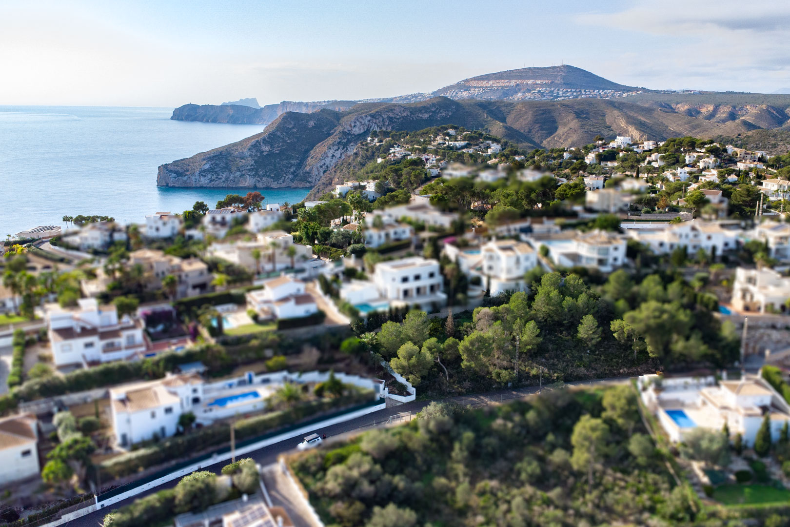 Luchtfoto met tilt-shift effect van de woonwijk Granadella-Ambolo, met witte villa's tussen de pijnbomen en de rotsachtige kustlijn van Jávea.