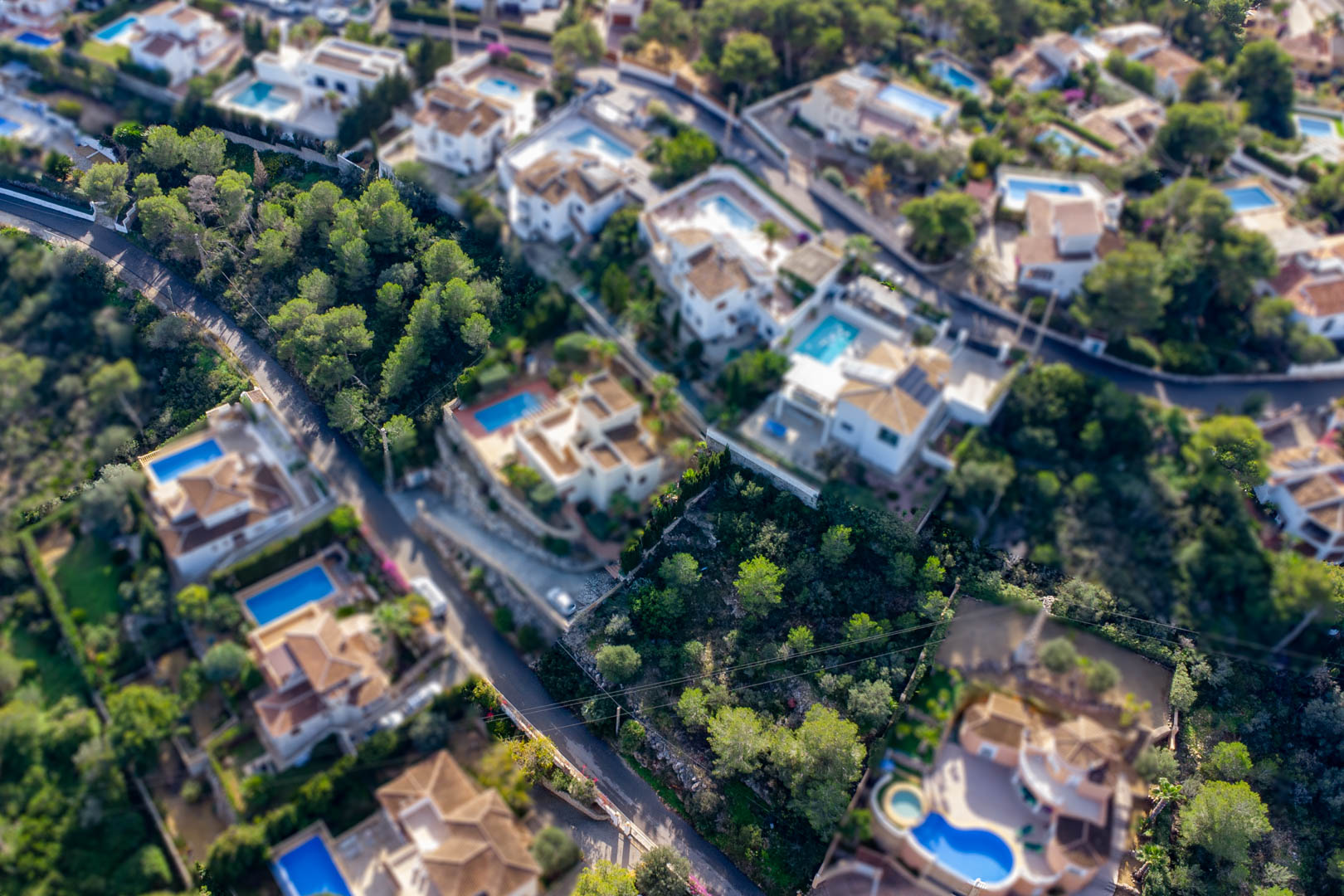 Luchtfoto van het bouwperceel in Granadella-Ambolo, gelegen tussen bestaande villa's met zwembaden en omgeven door volwassen pijnbomen.