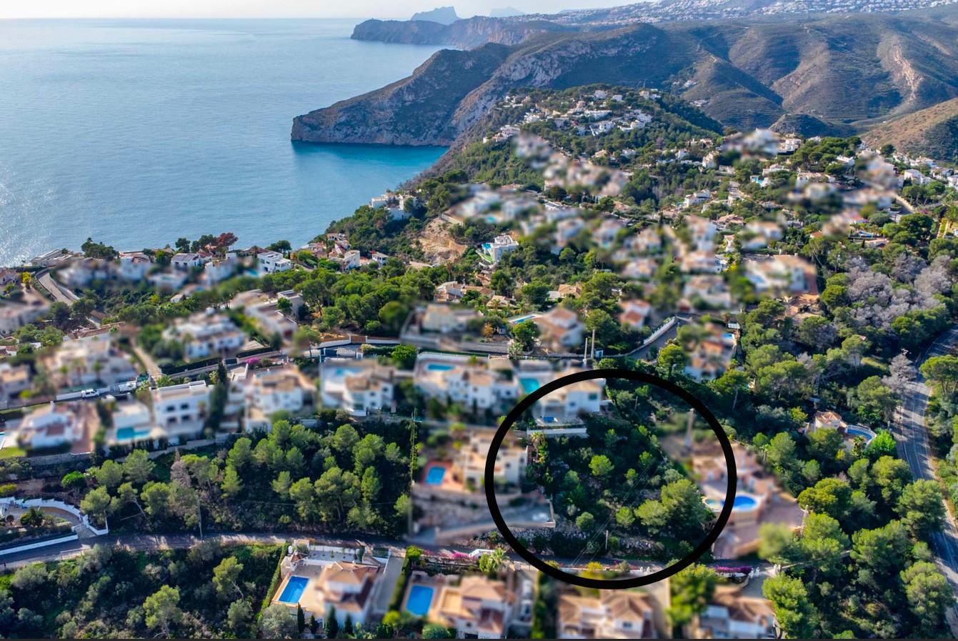 Luchtfoto van het perceel van 1042 m² omgeven door pijnbomen in de wijk Ambolo, met vrij uitzicht op de Middellandse Zee en de kustlijn van Jávea.