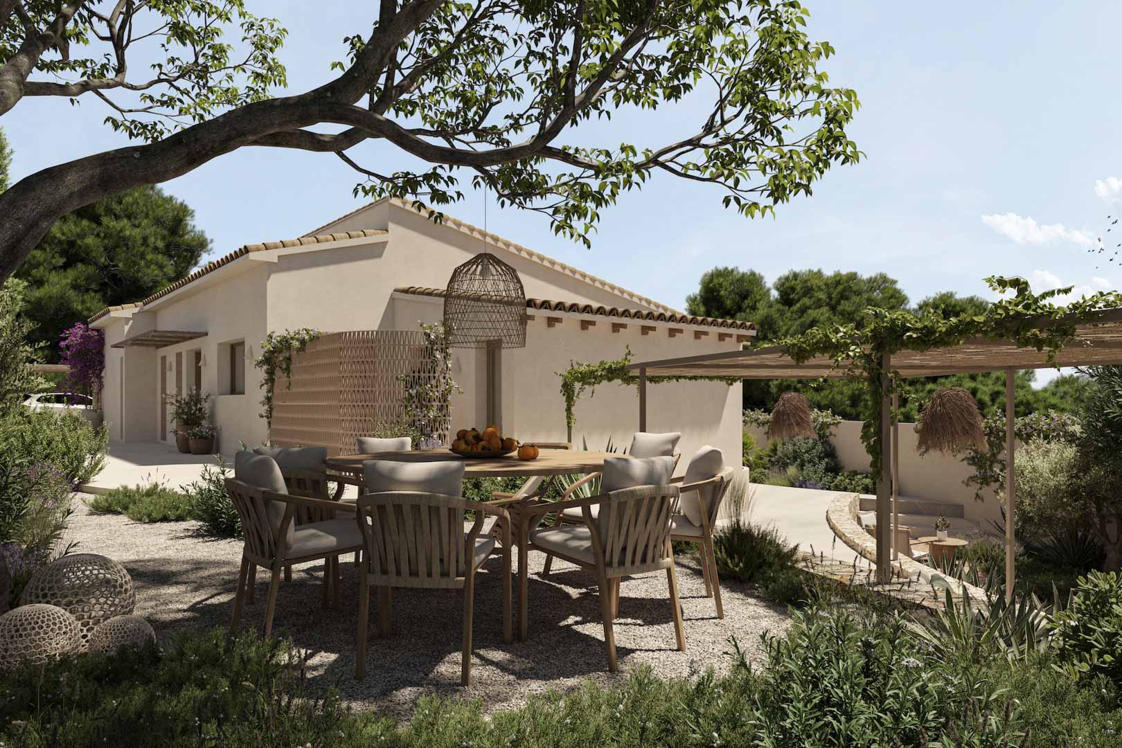 Buiteneethoek met een ronde houten tafel en gevlochten stoelen op een grindterras, omgeven door een mediterrane tuin met een begroeide pergola.