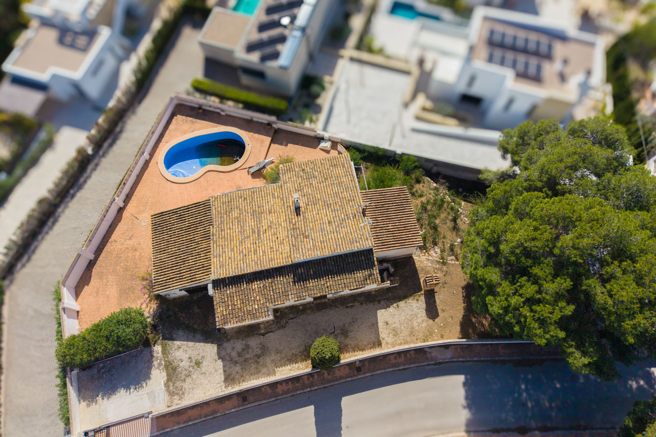 Luchtfoto van de villa met het terracotta pannendak, het organisch gevormde zwembad en het vlakke perceel in een rustige woonwijk.