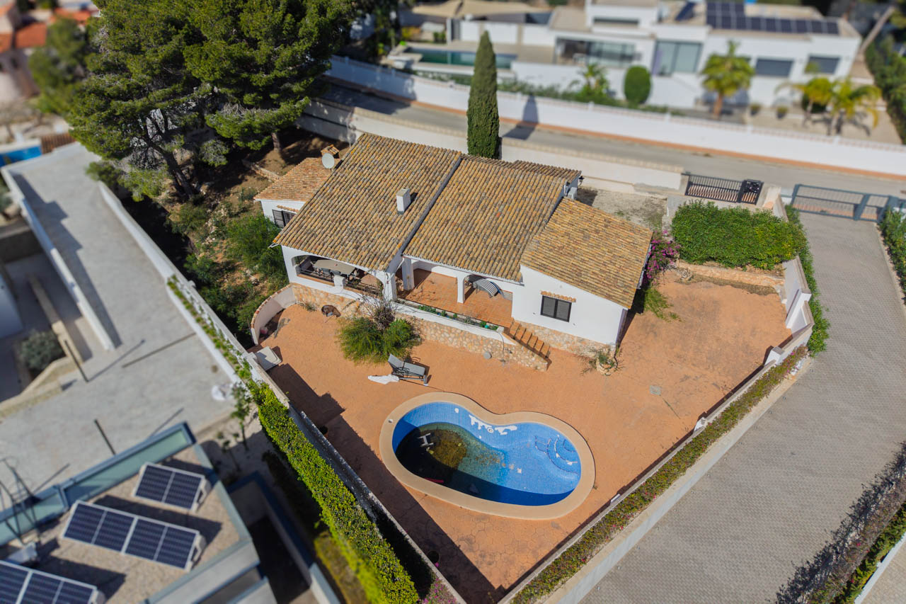 Luchtfoto van de villa met het vlakke perceel, het niervormige zwembad en de mediterrane architectuur met karakteristieke pannendaken en ruime terrassen.