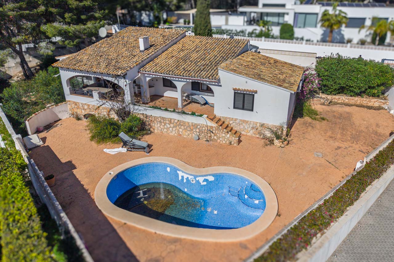 Luchtfoto van de villa met niervormig zwembad, ruime betegelde terrassen en overdekte veranda's met bogen. De woning heeft natuurstenen muren en een traditioneel pannendak.