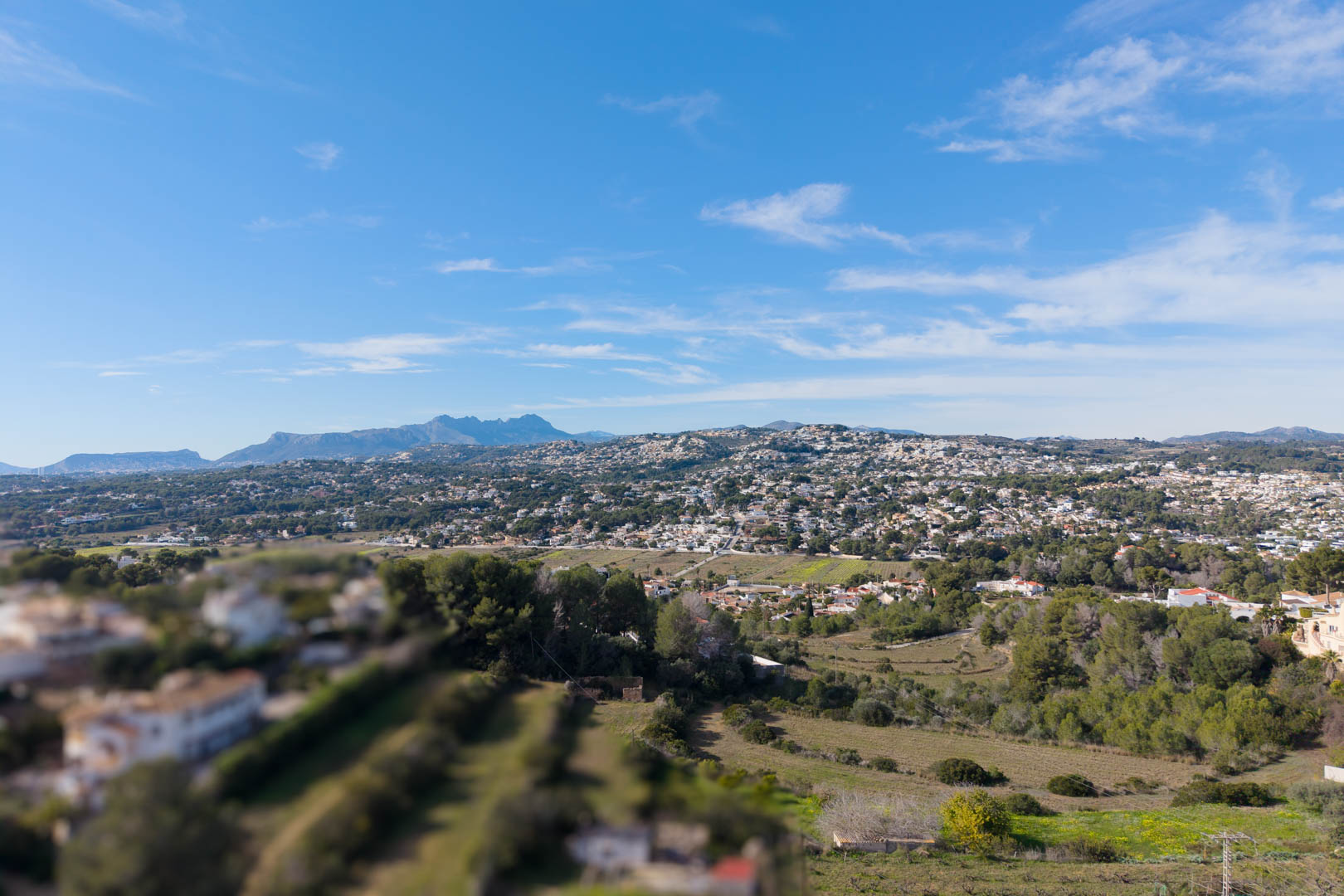 Verhoogd panoramisch uitzicht over de vallei van Moraira, met woonwijken te midden van het mediterrane landschap en bergen aan de horizon.