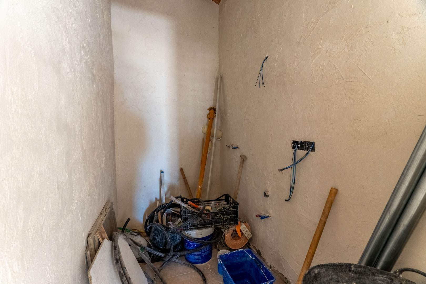 Binnenruimte in renovatie met gestuukte muren, zichtbare elektrische bedrading en diverse bouwmaterialen voor de verdere afwerking.
