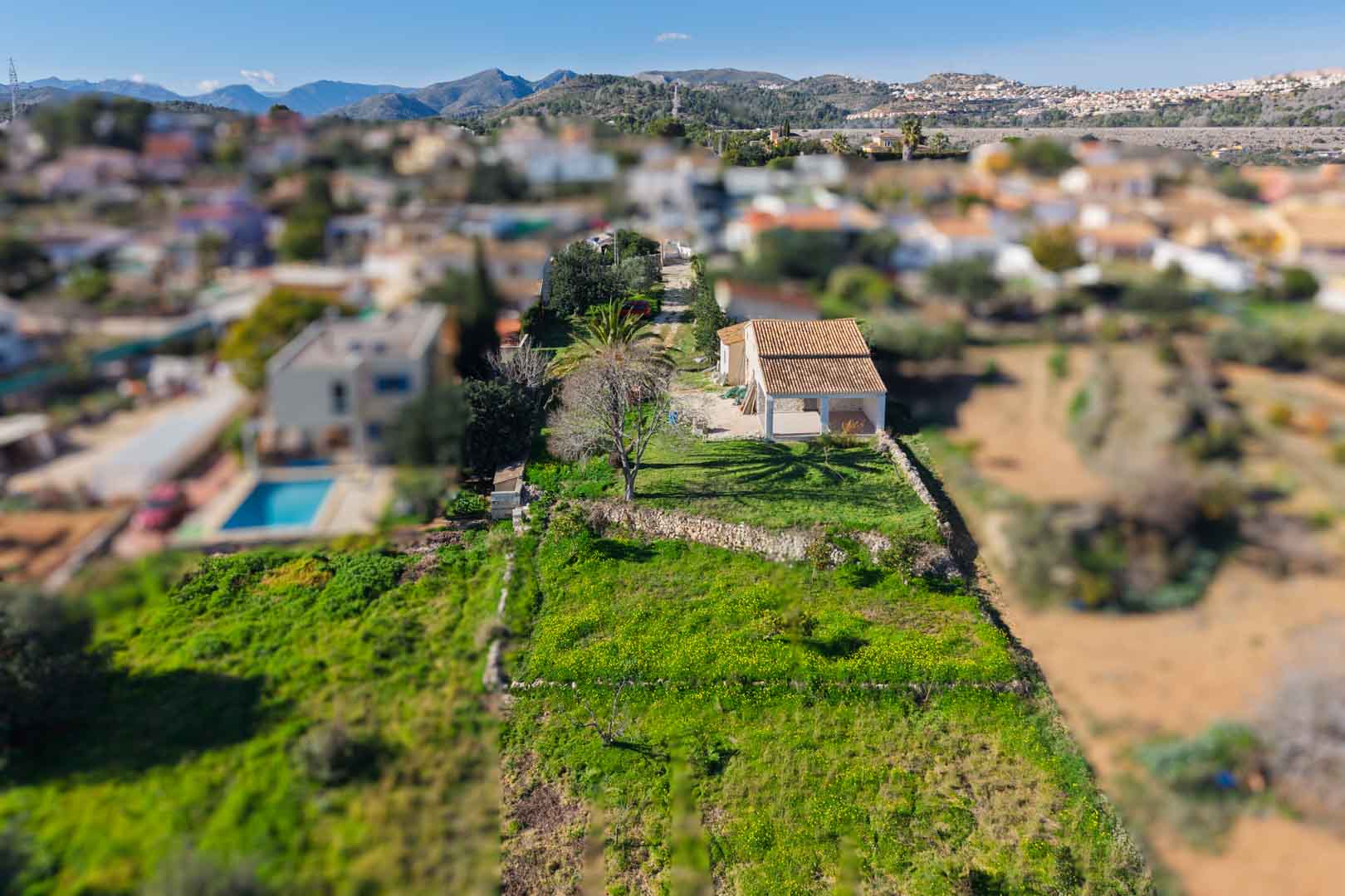 Luchtfoto van de finca met het vernieuwde pannendak en naya, gelegen op een langgerekt perceel met droge stenen muren en uitzicht op de omliggende bergen.
