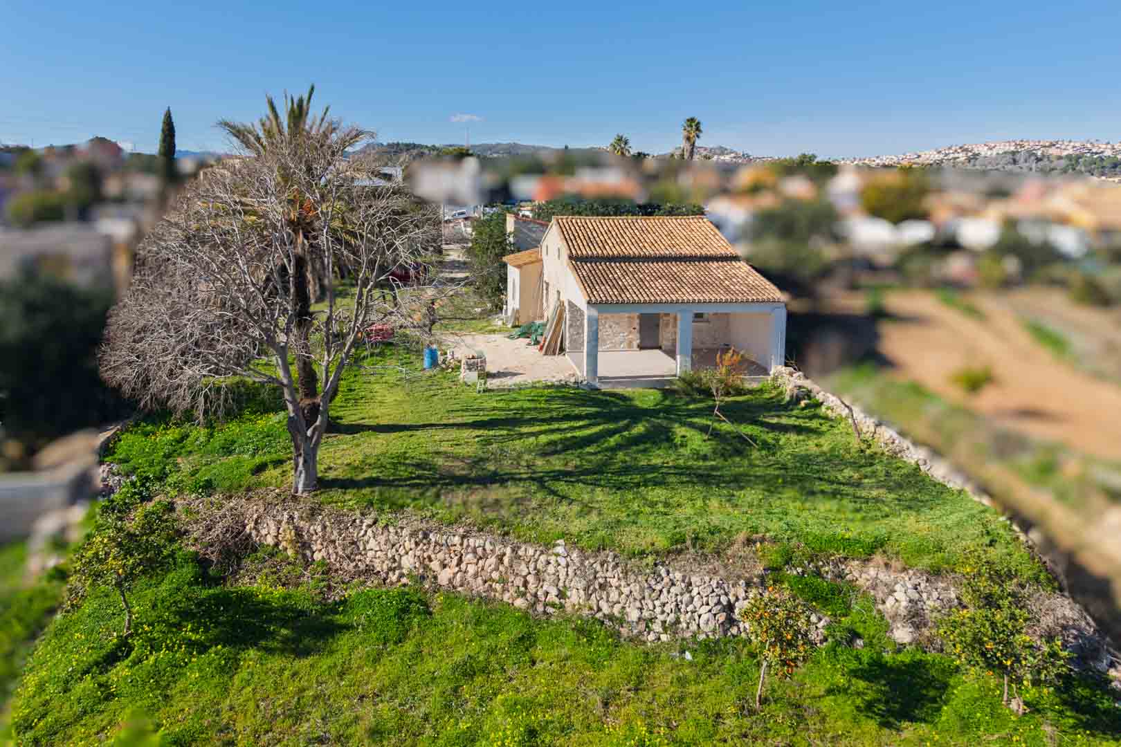 Luchtfoto van de traditionele finca met een gerenoveerd pannendak, droge stenen muren en een ruime naya, gelegen op een groen perceel met fruitbomen.