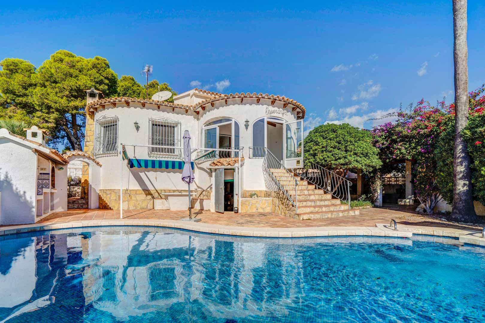 Exterieur van de villa met privézwembad, witte ronde gevel en stenen trap naar het glazen terras, gelegen in een volgroeide mediterrane tuin.