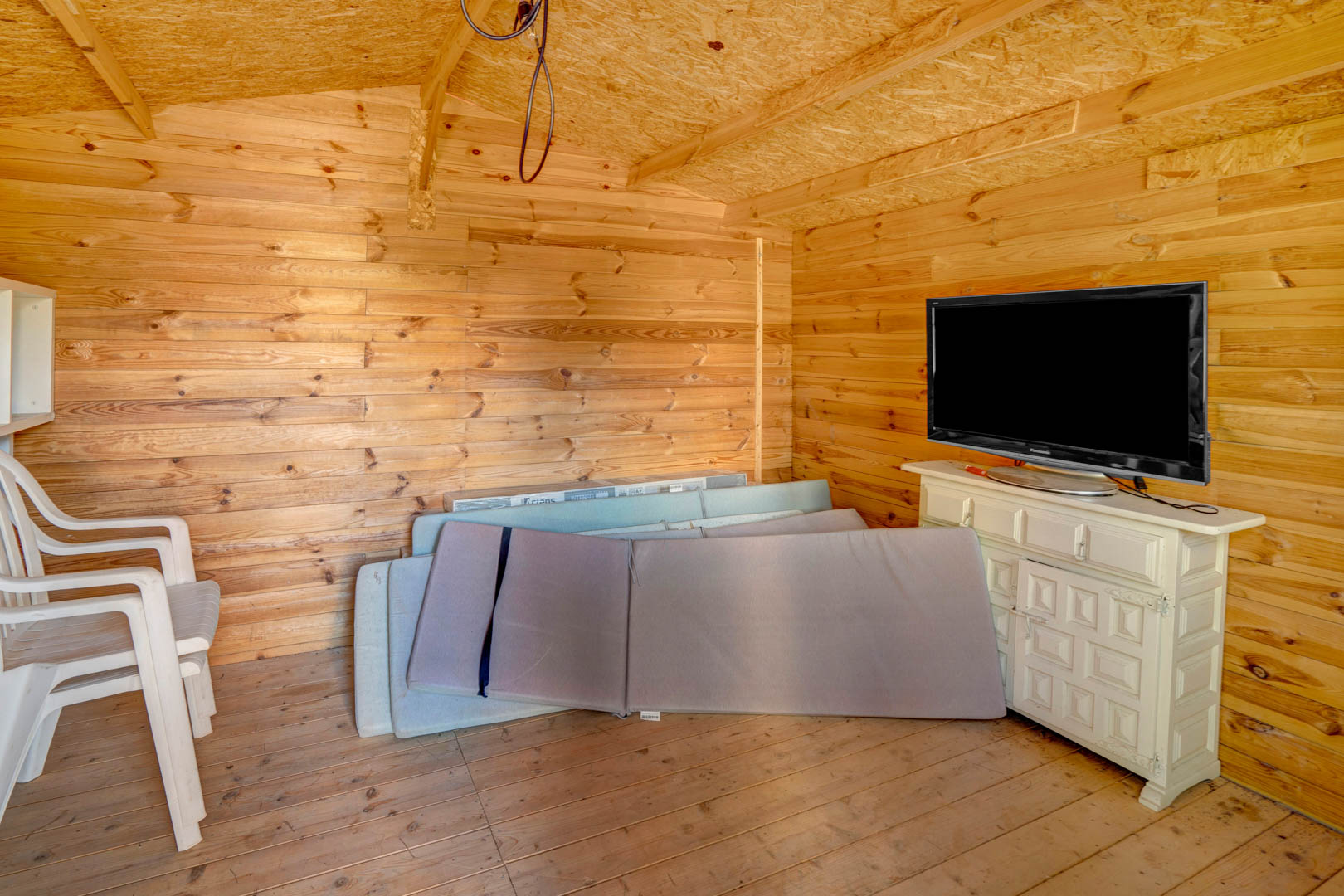 Houten tuinhuis of berging met grenen wanden, voorzien van een dressoir met televisie en opbergruimte voor kussens van tuinmeubilair.