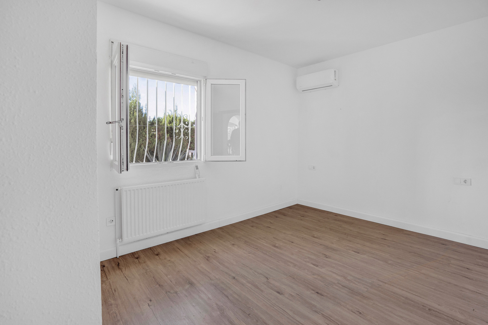 Lichte slaapkamer met laminaatvloer in houtlook, voorzien van een radiator voor centrale verwarming en een split-airconditioningsysteem.