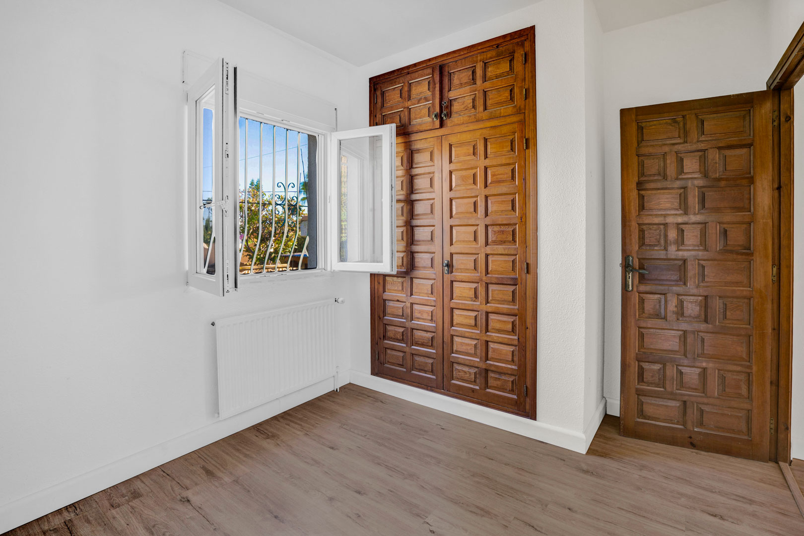 Slaapkamer met een ingebouwde houten kledingkast met paneeldeuren, laminaatvloer, radiator voor centrale verwarming en raam met natuurlijk licht.