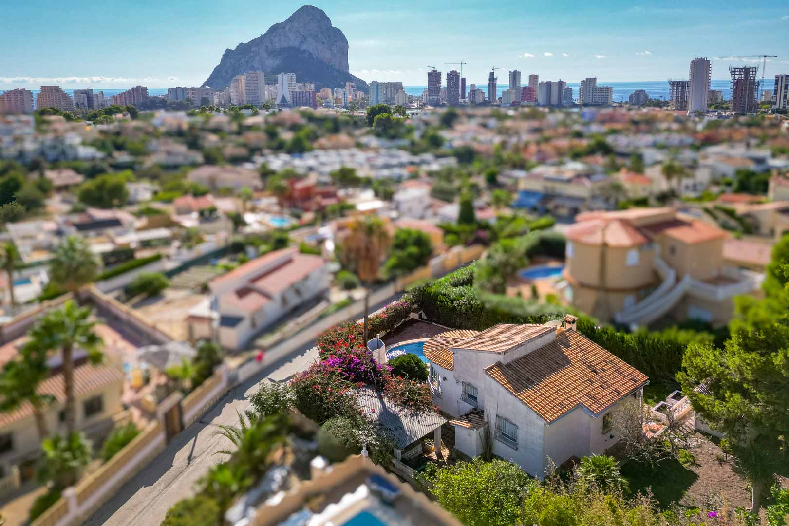 Verhoogd zicht op de villa met privézwembad en tuin, met een panoramisch uitzicht op de Peñón de Ifach en de skyline van Calpe.
