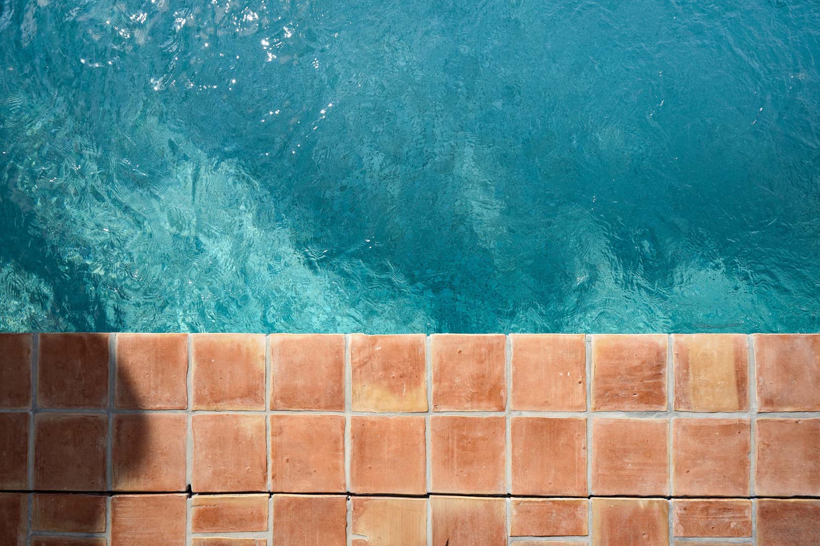 Bovenaanzicht van de zwembadrand met natuurlijke terracotta tegels en helder turquoise water, kenmerkend voor de mediterrane stijl van de woning.