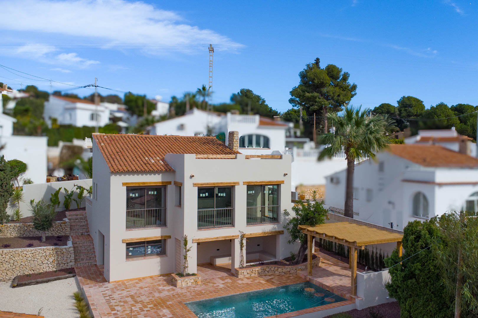Buitenaanzicht van de mediterrane villa met grote raampartijen, terracotta dak, privézwembad met houten pergola en natuurstenen muren.