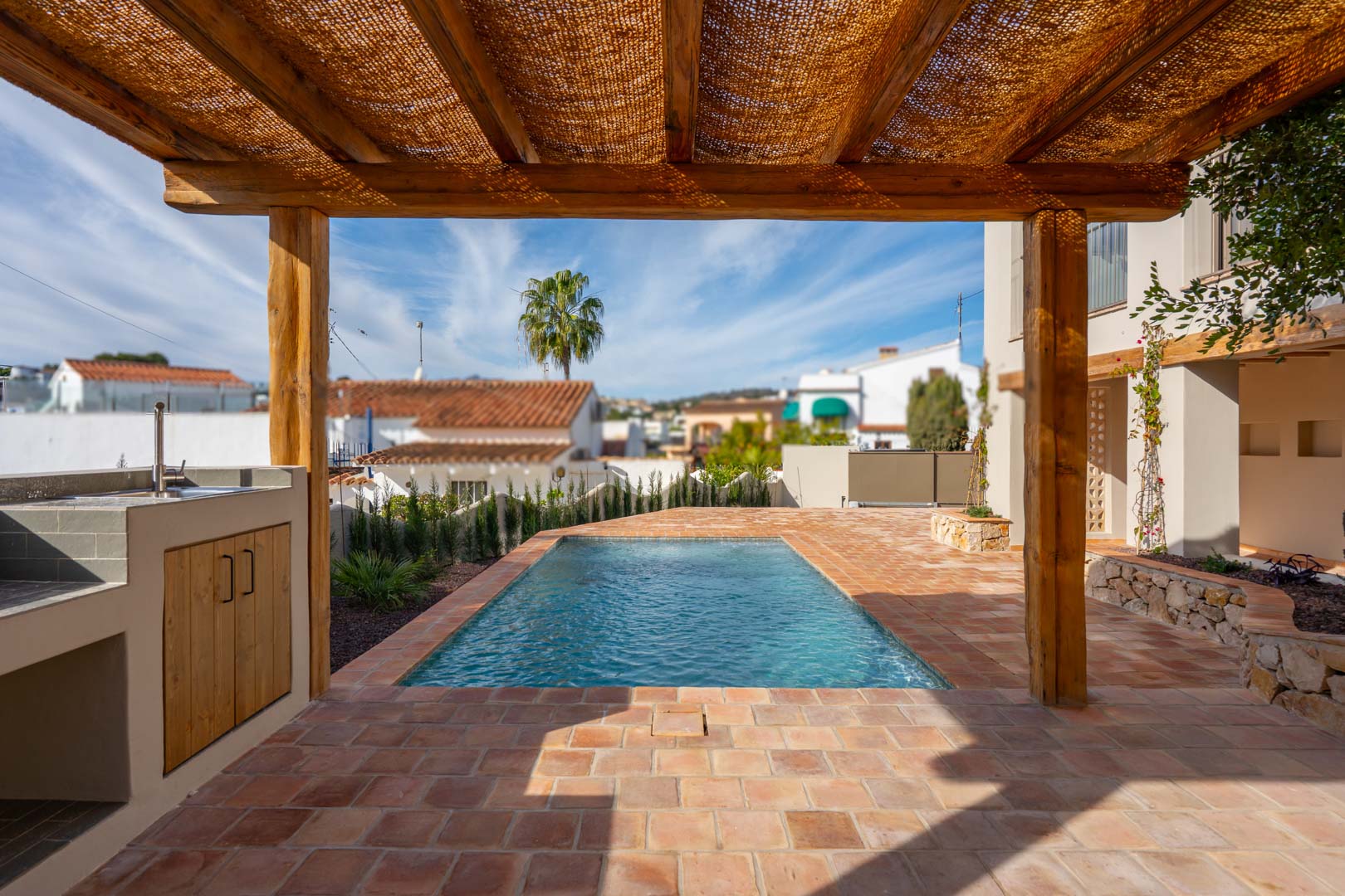 Buitenterras met terracotta tegels, een houten pergola en barbecueplaats naast het nieuw gebouwde zwembad in een mediterrane omgeving.