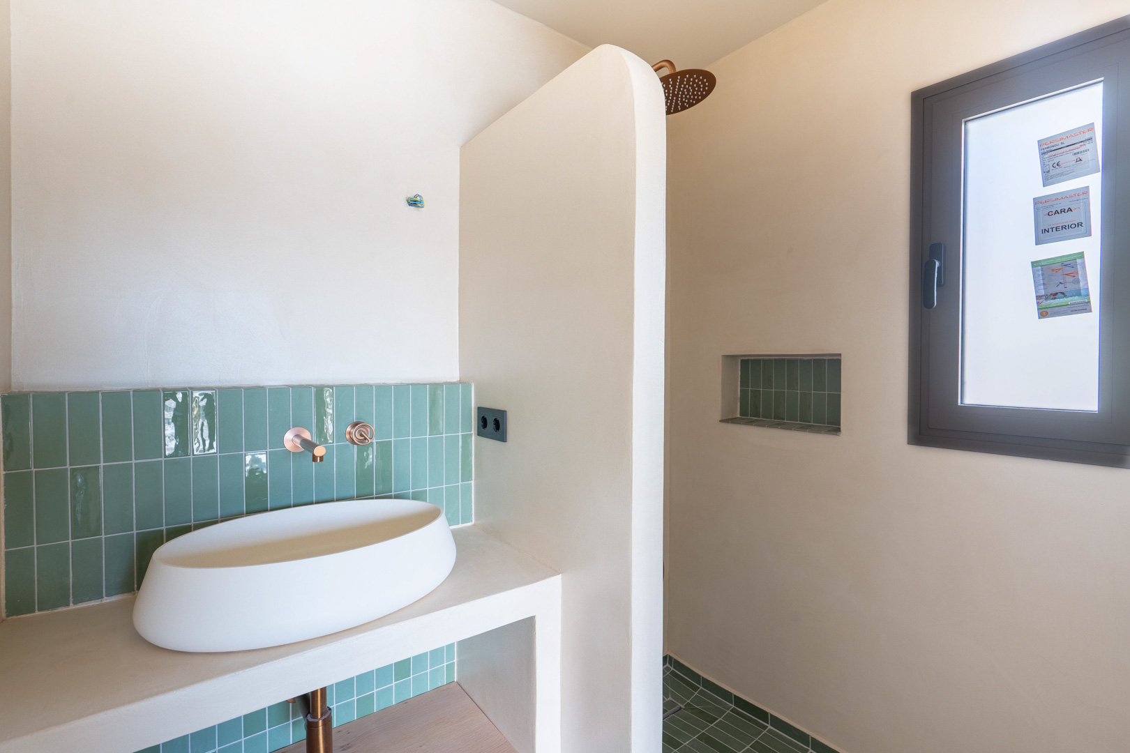 Designbadkamer met opzetwastafel, koperen inbouwkranen en verticale groene tegels. Inloopdouche met ingebouwde nis en afwerkingen in natuurlijke Matteo Brionni klei.