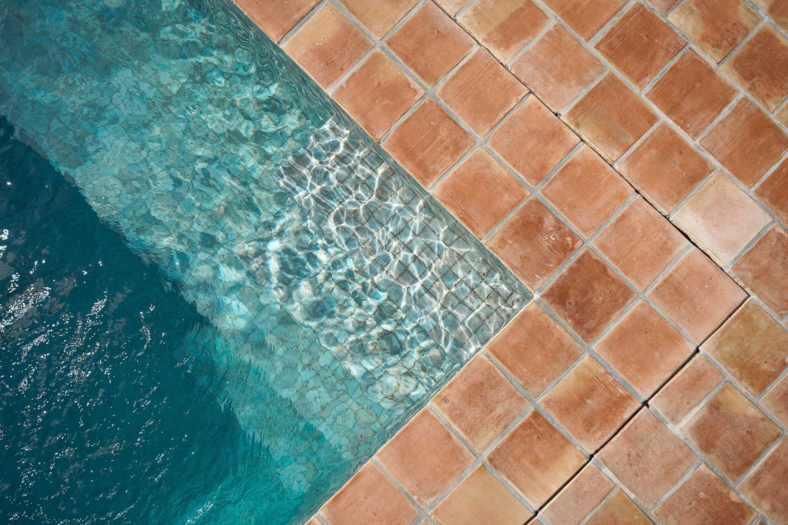 Detail van de zwembadhoek met authentieke terracotta tegels die prachtig contrasteren met het heldere turquoise water en de natuurlijke lichtinval.
