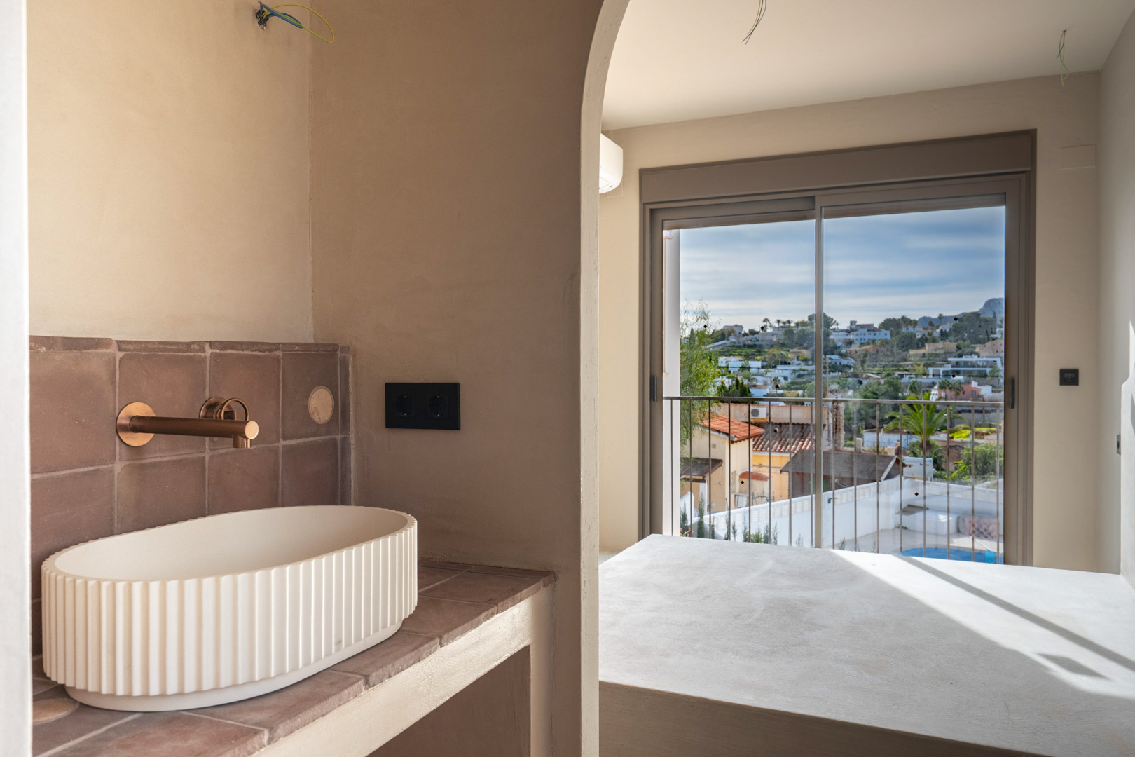 Ensuite badkamer met geribbelde opzetwaskom en koperen kranen, via een boog verbonden met de slaapkamer en het balkon met weids uitzicht.