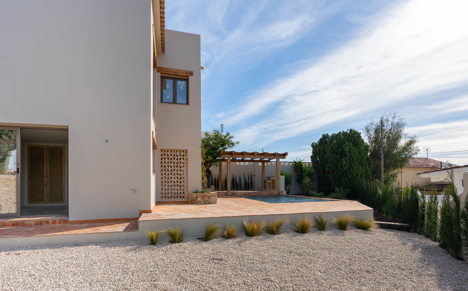 Exterieur van de villa met terracotta terras, nieuw gebouwd zwembad en houten pergola boven de barbecueplaats, omgeven door een onderhoudsvriendelijke grindtuin.