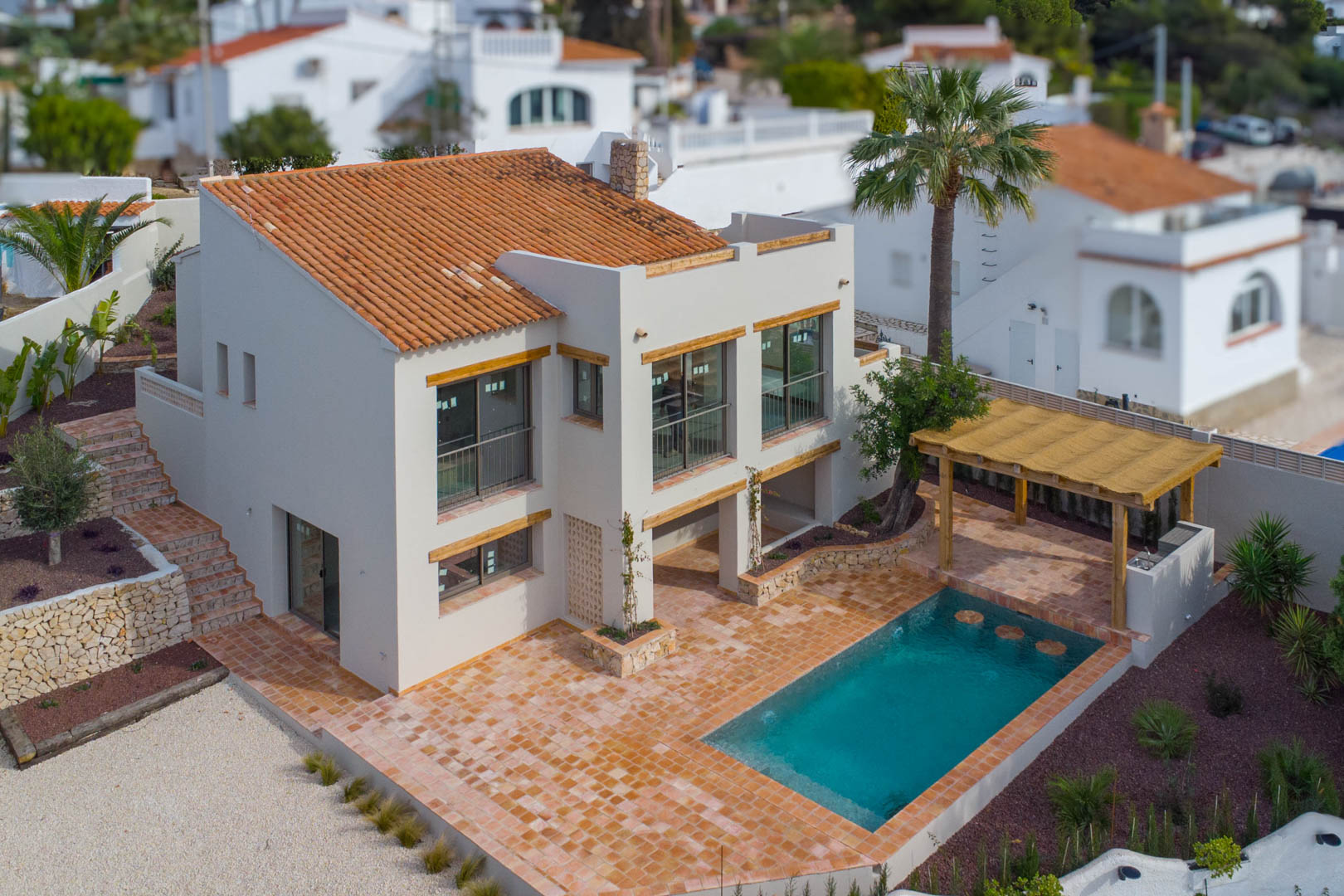 Luchtfoto van de villa met nieuw zwembad, ruim terras in terracotta en een houten pergola met buitenkeuken en barbecueplaats in de tuin.
