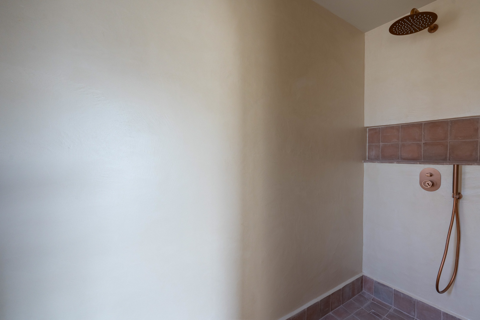 Moderne douche met Matteo Brioni kleiwanden, koperkleurige kranen en terracotta tegels voor een natuurlijke, mediterrane uitstraling.