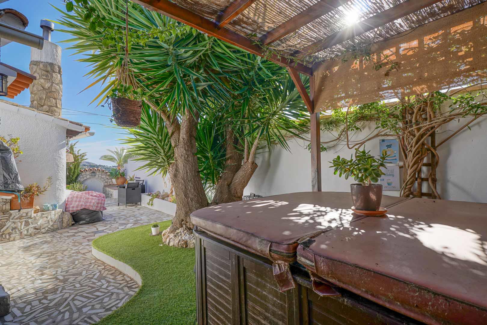 Buitenterras met een overdekte jacuzzi onder een houten pergola, gelegen in een onderhoudsvriendelijke tuin met natuurstenen bestrating en beplanting.
