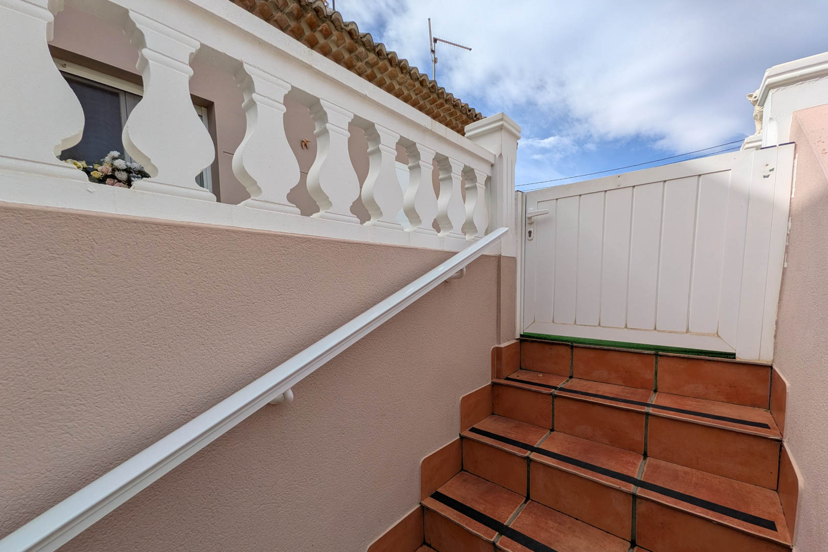 Externe toegangstrap met terracotta tegels, antislipstrips, witte leuning en klassieke balustrade die leidt naar de toegangspoort op de bovenverdieping.