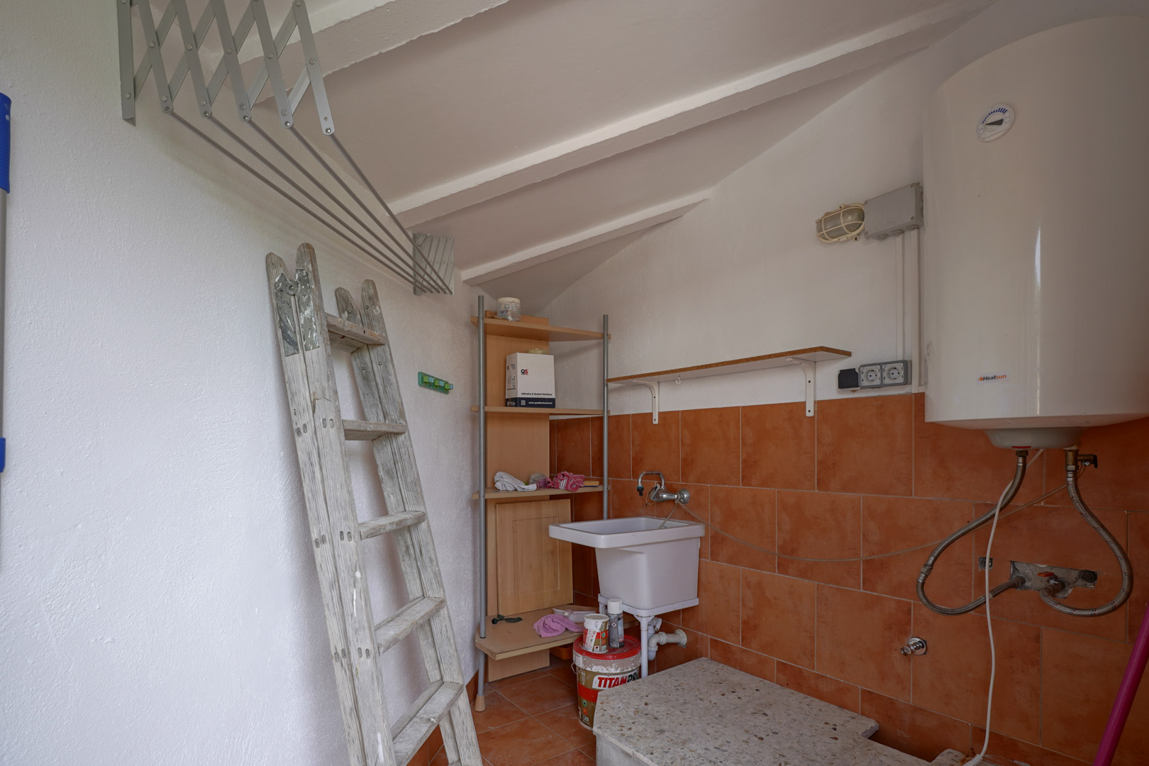 Functionele wasruimte en berging met schuin plafond, elektrische boiler, uitstortgootsteen en uittrekbaar wanddroogrek.