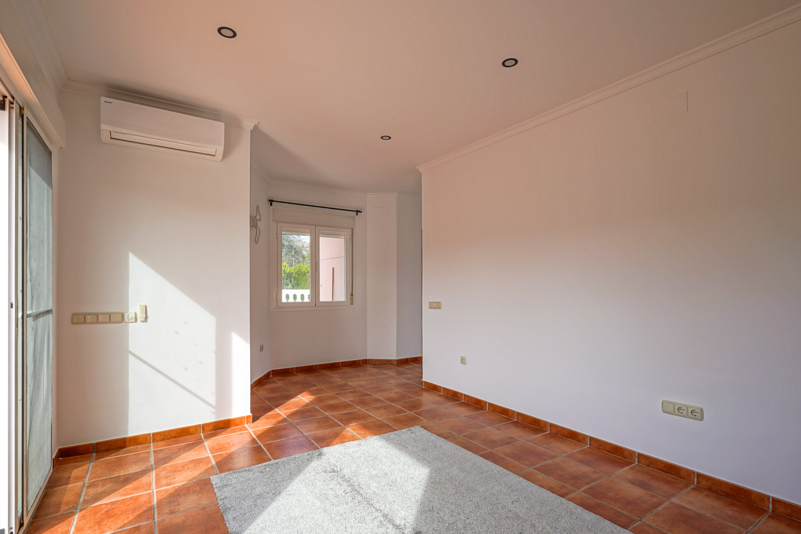 Lichte woon-eetkamer met rustieke terracotta vloertegels, split-airconditioning en directe toegang tot het buitenterras via glazen deuren.
