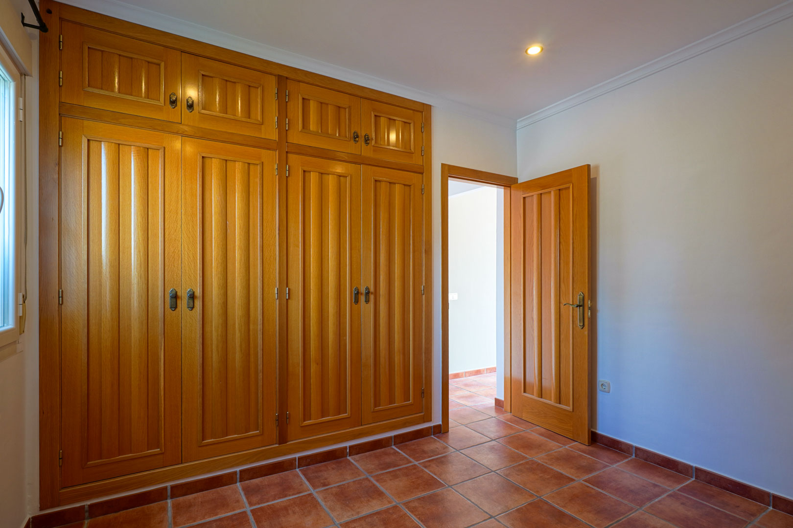 Slaapkamer met een grote kamerhoge houten inbouwkast, traditionele terracotta tegelvloer en inbouwspots in het plafond.