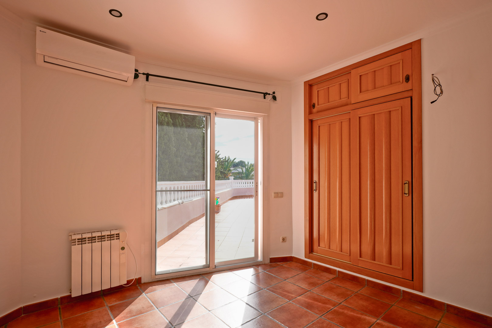 Slaapkamer met ingebouwde houten kledingkast, terracotta vloertegels en toegang tot het terras. Voorzien van airconditioning, elektrische radiator en inbouwspots.