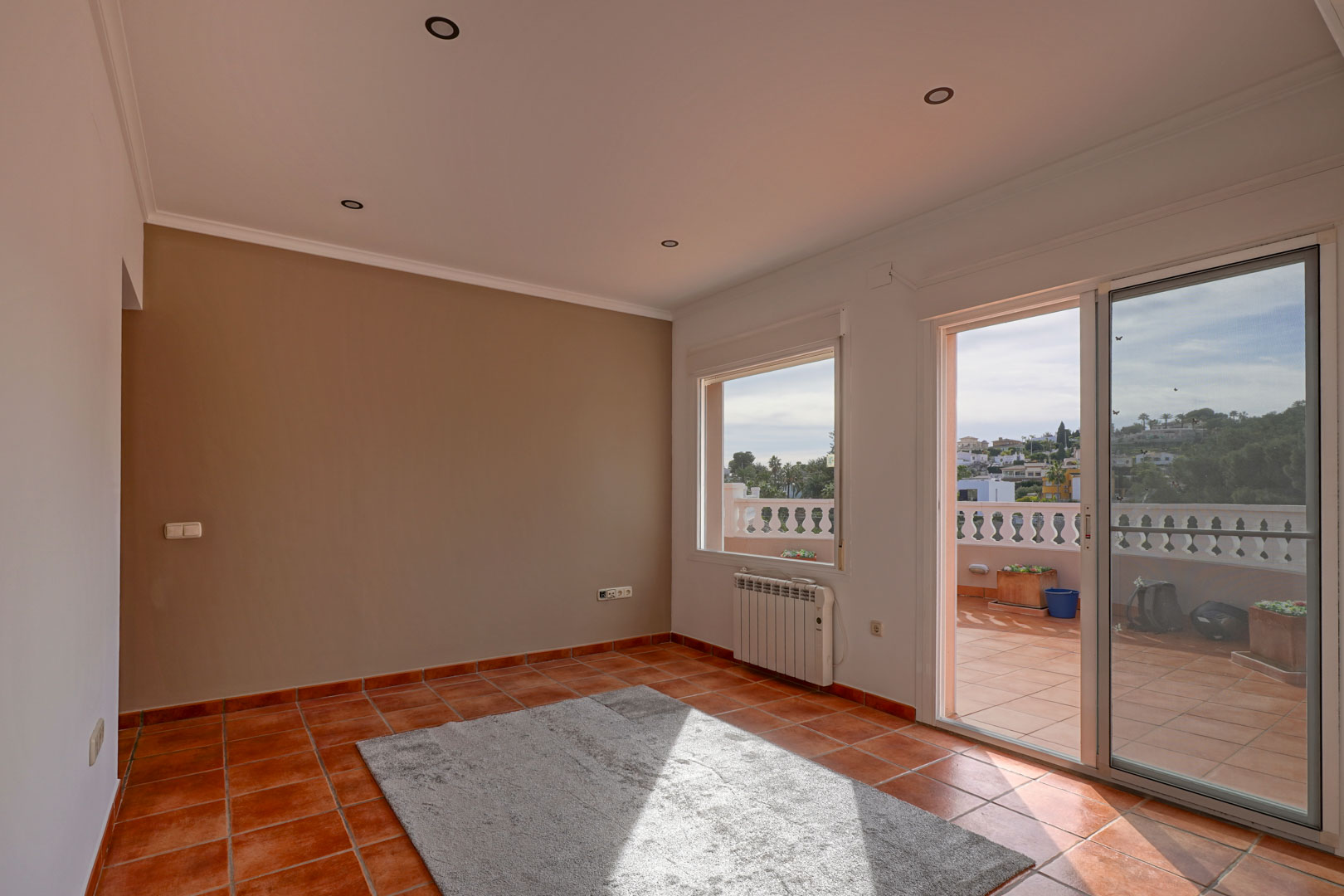 Woonkamer met terracotta tegelvloer, inbouwspots en toegang tot een ruim terras. Voorzien van een elektrische radiator en een stijlvolle accentmuur.