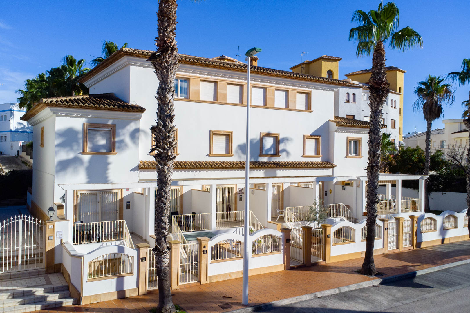 Buitengevel van triplex woningen in mediterrane stijl met witte muren, stenen raamlijsten en privéterrassen aan de straatzijde.